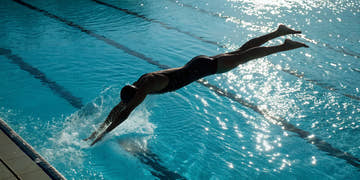 Competitive swimmer in a performance suit diving off the blocks into a pool.