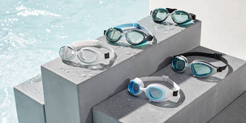 An assortment of the best fitness goggles for swimming, displayed in various colors by the water.