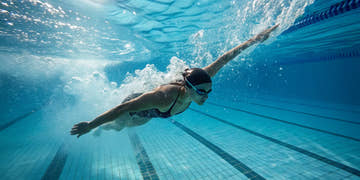 A swimmer in a competitive swim suit racing underwater in a pool.