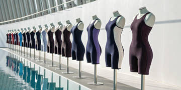 A collection of high-performance women's swim meet suits on mannequins by a pool.
