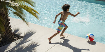 Young boy in colorful swim trunks running by the pool.