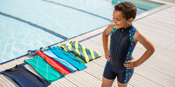 A young boy in competitive swimwear with a selection of boys' jammers and briefs by the pool.