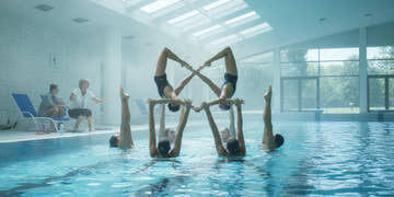 Artistic swimmers practicing a synchronized routine in a bright indoor pool