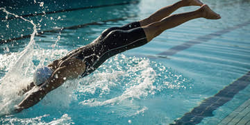 Male swimmer wearing competition jammers dives off the starting block for a race.
