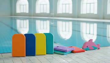 A selection of colorful swim kickboards lined up beside a swimming pool, including rectangular, contoured, and junior-sized boards