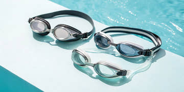 Three pairs of Speedo goggles with different lenses and straps on a poolside.