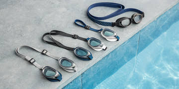 Various styles of swimming goggles for racing, training, and recreation by a pool.