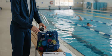 Swim coach organizing a whistle, stopwatch, clipboard, and training gear beside a pool