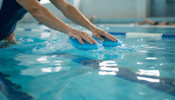 Swimmer using blue hand paddles in a pool during training, hands catching water with proper technique