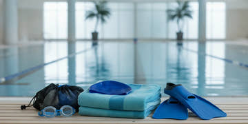 Swim training essentials including goggles, a cap, towel, and fins arranged beside a pool