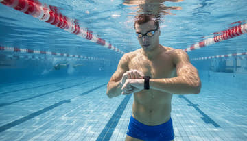Swimmer checking a sports watch beside an indoor lap pool
