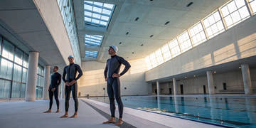 Men's tech suits on three swimmers preparing for a race at the pool.