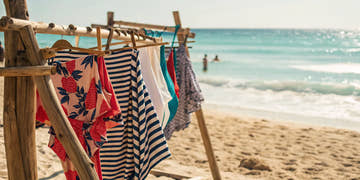 A variety of swimwear from an online store hanging on a rack by the ocean.