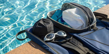 A set of competitive swim gear with goggles and a swim cap by the pool.