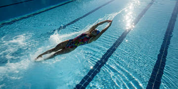 Swimmer wearing a technical racing suit dives from the starting block into a swimming pool.
