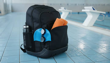 A sleek competitive swim backpack packed with gear on an indoor pool deck