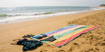 A colorful swimsuit and towel on the sand, representing the many options for where to buy swimwear.