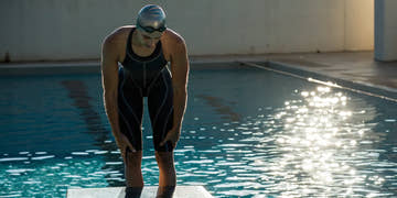 Swimmer in a tech racing suit on a starting block, ready for competition.